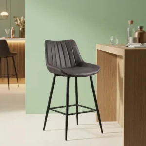 Dark gray leatherette barstool with vertical channel-tufted low backrest, contoured bucket seat, black tapered steel legs, and integrated footrest crossbars.