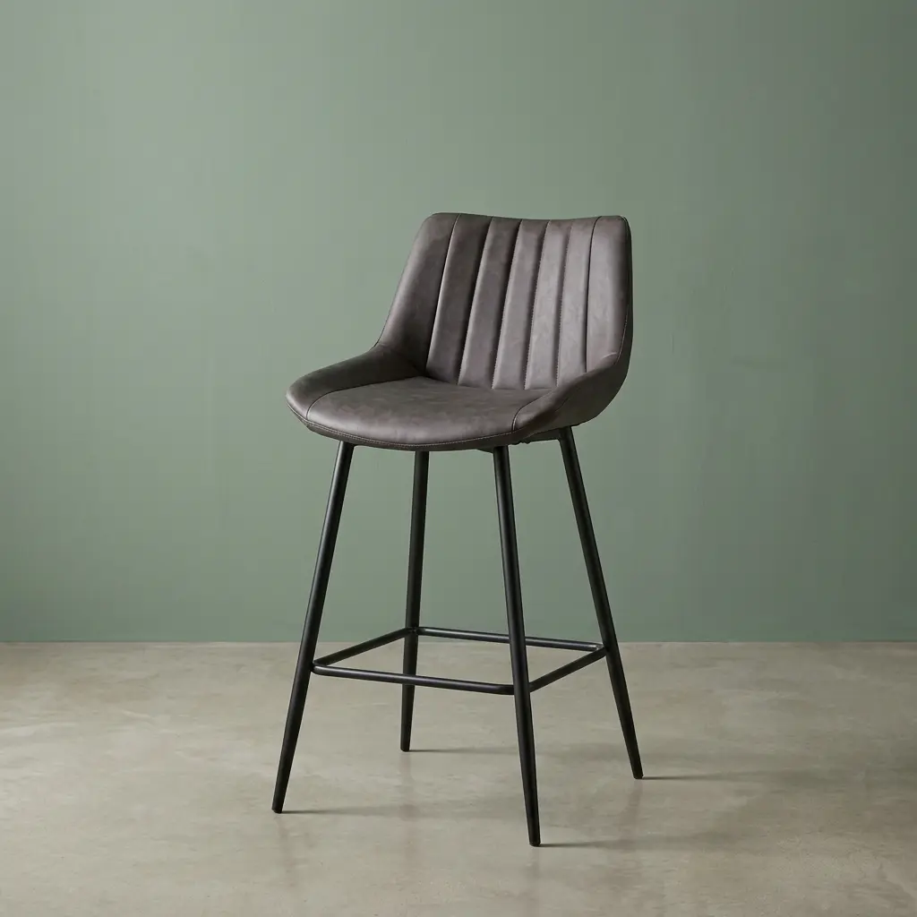 Dark gray leatherette kitchen barstool with vertical channel-tufted low backrest, bucket seat design, black tapered metal legs, and integrated square footrest.