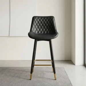 Black leather kitchen counter barstool with diamond-quilted bucket seat, black tapered legs, brass footrest, and gold leg caps.