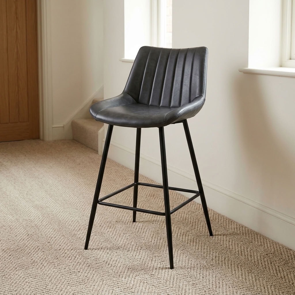 Gray leather counter barstool with vertical channel-stitched backrest, bucket seat, black metal tapered legs, and integrated footrest crossbars.
